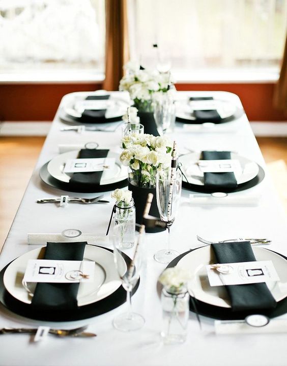 a casual monochromatic talescape with black chargers, napkins, vases and white blooms and all the rest in white