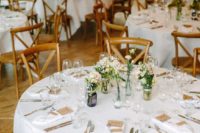a chic barn wedding table with white linens, wildflowers in jars, candles and tags and cards