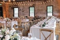 a chic barn wedding tablescape with white linens, white blooms and greenery and silver cutlery and chargers
