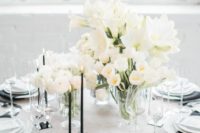 a chic black and white tablescape with a black napkin and thing candles, white blooms and porcelain