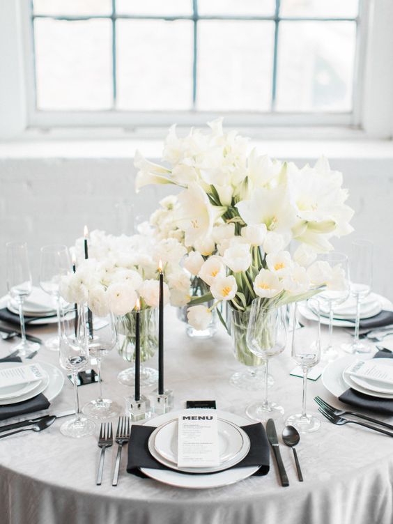 a chic black and white tablescape with a black napkin and thing candles, white blooms and porcelain