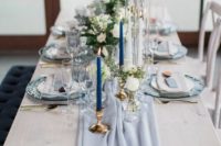 a chic wedding tablescape with a powder blue runner and cards, with navy candles, neutral blooms and greenery