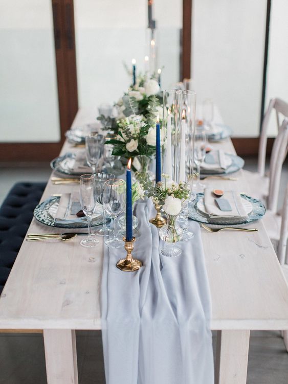 a chic wedding tablescape with a powder blue runner and cards, with navy candles, neutral blooms and greenery