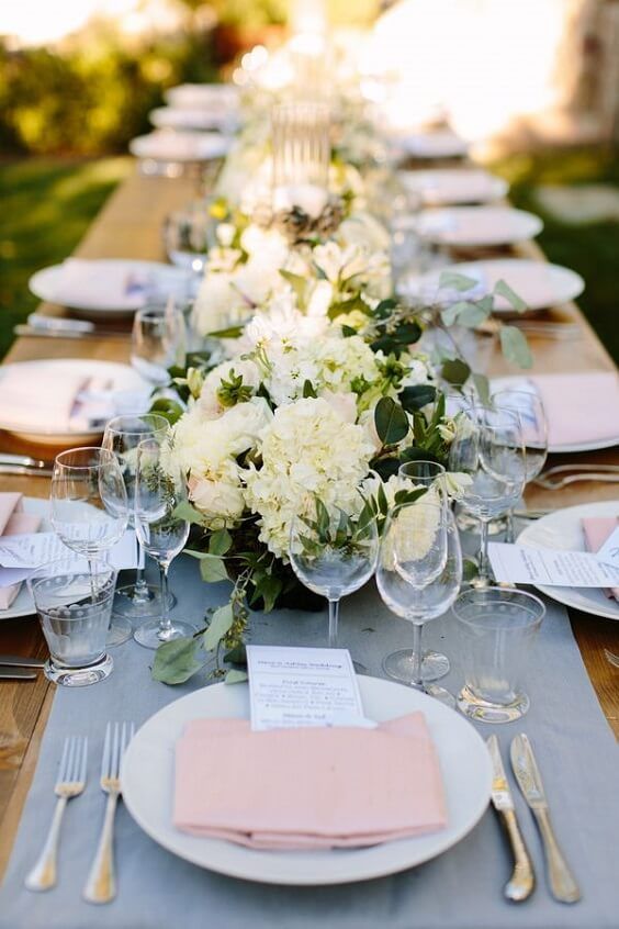 a chic wedding tablescape with a powder blue runner, neutral blooms and greenery, pink napkins and elegant menus