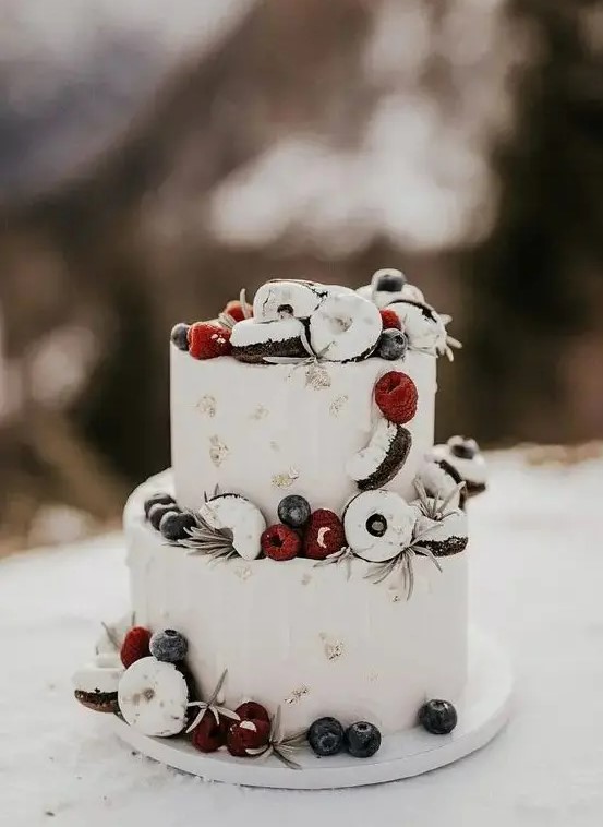 a chic white frosted wedding cake with gold leaf, white drip, berries and glazed donuts is amazing