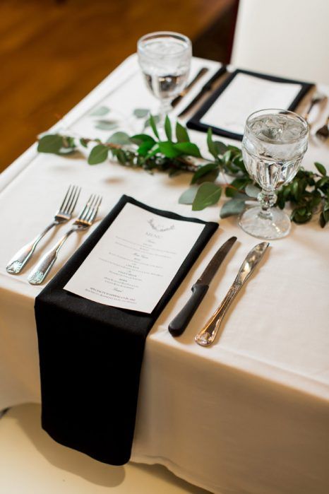 a chic yet simple black and white wedding tablescape with a greenery runner, black napkins and white menus