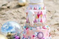 a colorful and crazy wedding cake with mismatching and bright detailed tiers, with colorful shards and a faux skull for a Burning Man wedding