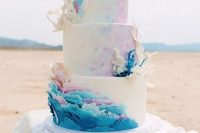 a colorful beach wedding cake with blue and pink watercolors, with colorful waves, corals and scales on the top tier