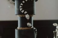 a creative All Hallows Eve black wedding cake with gold drip and black and white snakes is fabulous