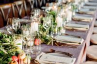 a fall barn wedding tablescape with a mauve tablecloth, greenery, apples and pillar candles