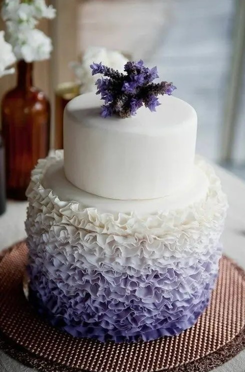 a fancy wedding cake with a white and ombre white to purple ruffle tier and with purple blooms on top is an amazing idea to rock