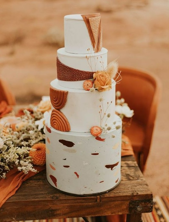 a fantastic boho wedding cake with white tiers, colorful brushstrokes, rust sugar detailing and some orange and dried blooms