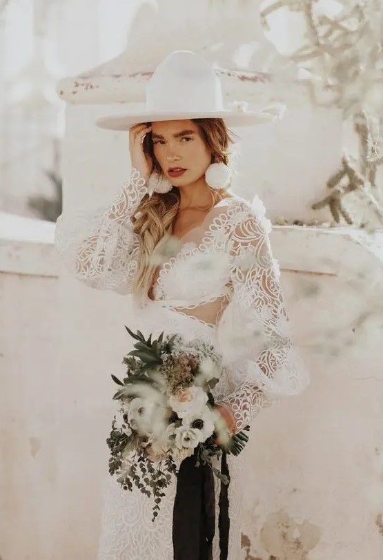 a fantastic bridal look with a boho lace mermaid wedding dress with puff sleeves, a white hat and statement pompom earrings
