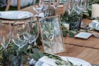 a fresh barn wedding tablescape with an uncovered table, a woven placemat, greenery and a framed table number