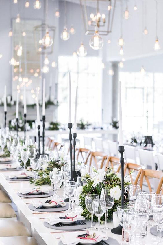 a fresh monochromatic tablescape with thin white candles in black candle holders, greenery and white bloom centerpeices and black menus
