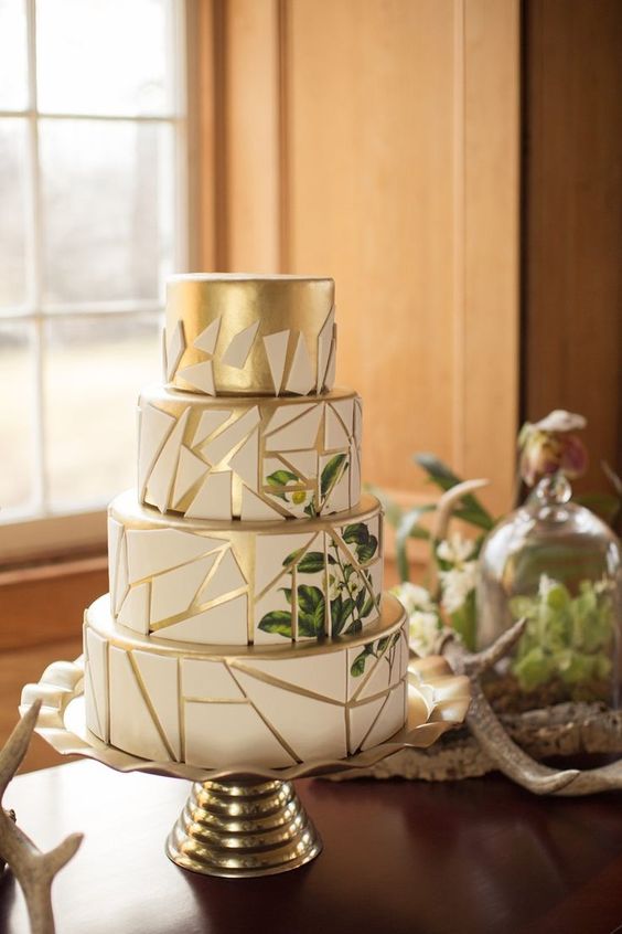 a gold and white wedding cake decorated with shards and with painted greenery and blooms is a stylish and lovely idea