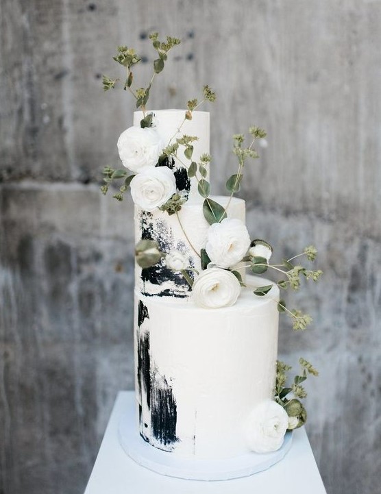 a gorgeous black and white brushstroke wedding cake decorated with white ranunculus and greenery