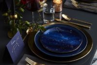a grey and navy table setting with gold cutlery, black candles and gold candle holders and a bold centerpiece with ffruits