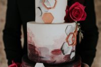 a jaw-dropping wedding cake with burgundy and black brushstrokes, white and copper hexagons and pink roses plus greenery