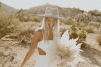 a modern boho bridal look with a plain fitting wedding dress with cutouts, a grey embellished aht and a cool dired weddin bouquet