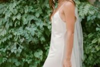 a modern bridal outfit with a silk slip wedding dress, a white hat with a veil and a beaded bag is an eye-catchy and chic idea