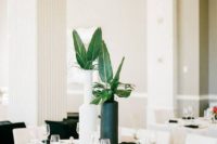 a modern tropical table setting with black candles, a black and white vase with tropical leaves and clear glasses