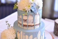 a naked wedding cake with powder blue drip, blue and white blooms and a wooden topper