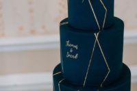 a navy and gold wedding cake with calligraphy and fresh blooms on top looks very chic