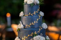 a navy wedding cake decorated with gold leaves, white blooms and berries