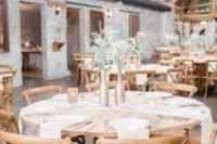 a neutral barn wedding table with neutral linens, metallic bottles with greenery and white blooms and simple cutlery