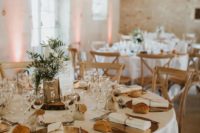 a neutral barn wedding table with shiny chargers, a greenery centerpiece on a wood slice, some candles and bread
