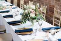 a neutral table setting with gold chargers, navy napkins and a cute neutral floral centerpiece