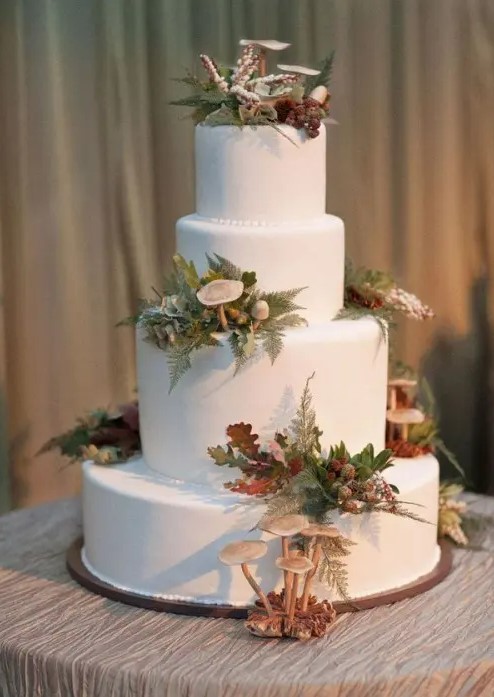 a pure white wedding cake topped with mushrooms, ferns, foliage and berries that are all edible