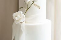 a refined and chic white wedding cake with a white rose branch with a gilded stem and a ribbon is gorgeous