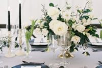 a refined black and white tablescape with a lsuh neutral floral centerpiece, black cutlery, plates and candles plus gold touches