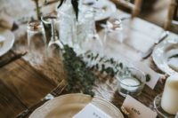 a romantic barn wedding tablescape with a lace runner, a greenery and wildflower centerpiece, white porcelain and touches of fir