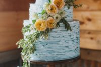 a ruffle powder blue wedding cake decorated with greenery and neutral and rust blooms