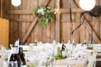 a simple barn wedding table with a greenery and lights runner, bottles and striped napkins