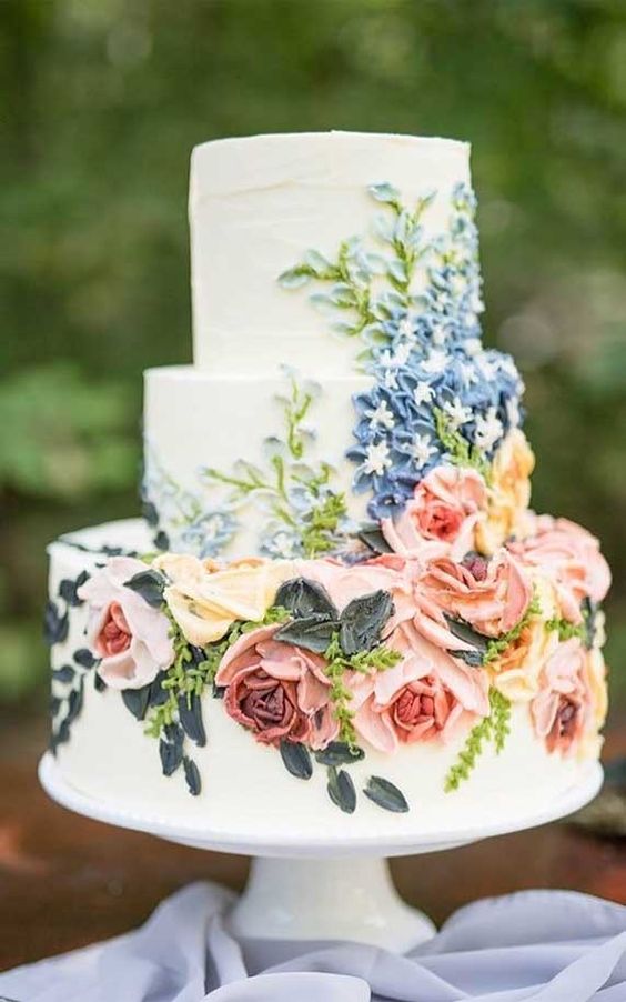 a sophisticated white wedding cake with pink and blue sugar blooms and greenery is a beautiful and chic idea for a spring or summer wedding