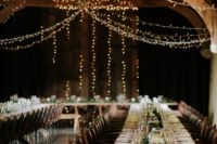 a stylish barn wedding table with a greenery runner, some candles and simpel plates and glasses