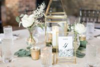 a stylish neutral wedding table with a gold candle lantern, a table number, white blooms and greenery and white linens