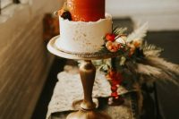 a two tone wedding cake with a rough edge, with a white and rust tier, gold leaf and fresh bright blooms and greenery