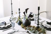 a unique black and white tablescape with silver chargers, black and white plates, white candles in black candle holders and black vases