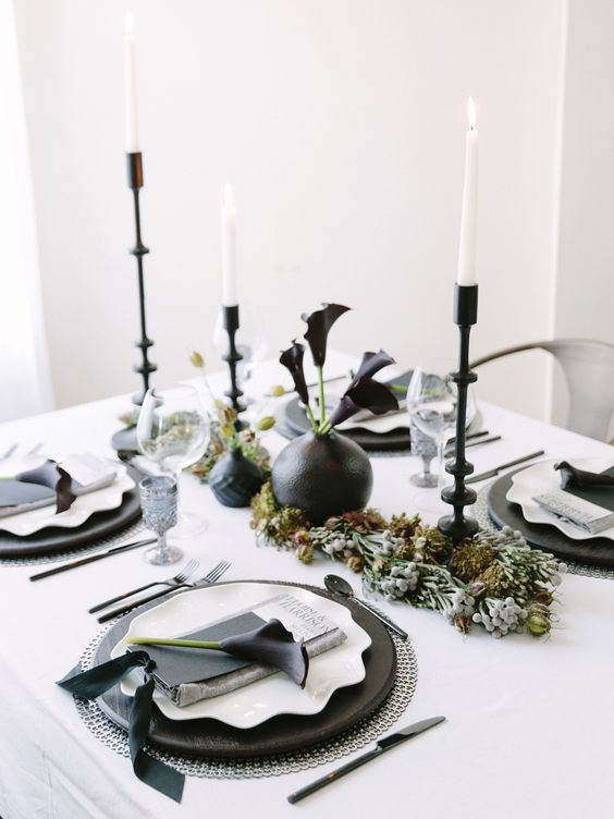 a unique black and white tablescape with silver chargers, black and white plates, white candles in black candle holders and black vases