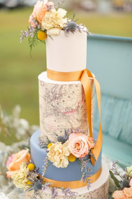 a vintage-inspired wedding cake with a blue and white tier, with a map tier and natural blooms and marigold ribbons