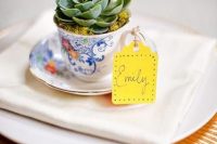 a vintage teacup with a succulent planted and a bright escort card is a fantastic and very eco-friendly wedding favor