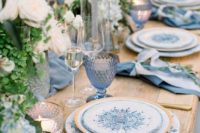a vivid wedding tablescape with blue glasses, napkins, printed plates and white blooms and greenery plus candles