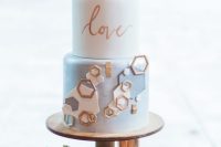 a white and light blue wedding cake with white, blue and copper hexagons, calligraphy and lovely gold himmeli toppers