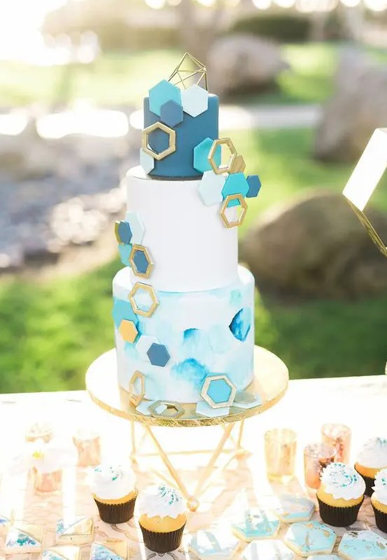 a white, light blue and navy wedding cake with a watercolor tier, a white and a navy one, gold, turquoise and navy hexagons