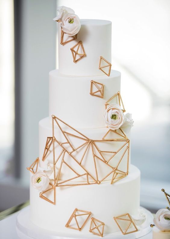 a white round wedding cake decorated with gold geometric touches and blush ranunculus is a stylish and refined idea for spring or summer
